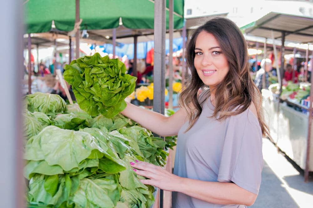 Portrait of beautiful young woman choosing green leafy vegetables in green market. Concept of healthy food shopping. Young woman buying vegetables at the green market.