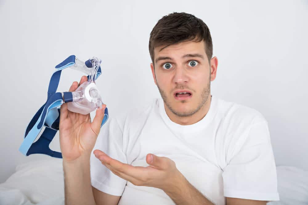 Close-up Of Shocked Young Man Holding CPAP Machine Mask