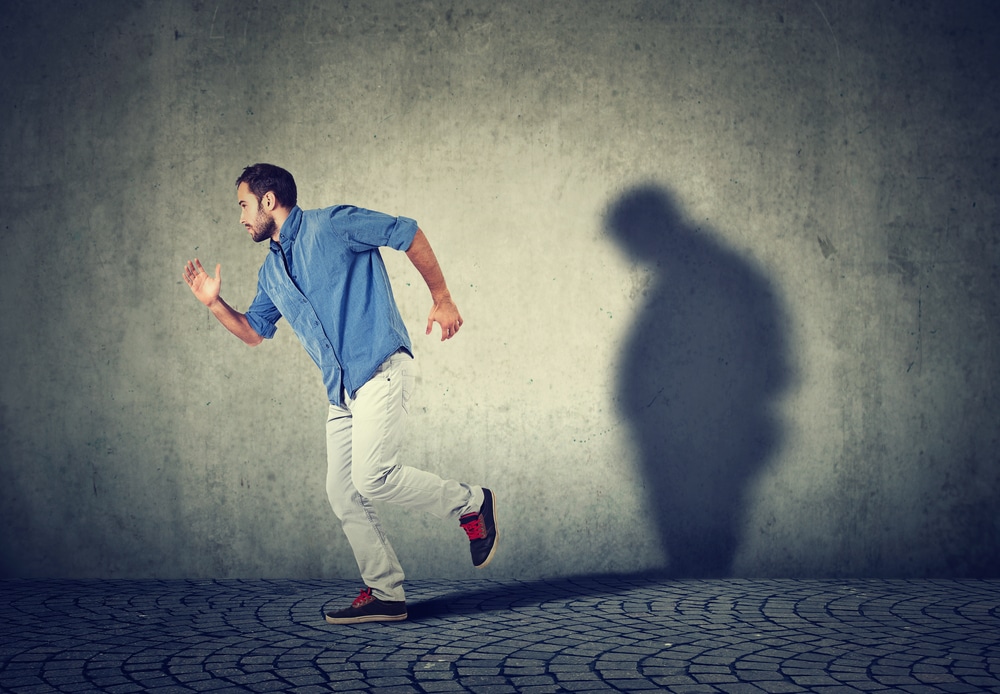 Man running away from his sad gloomy fat shadow on the wall. Mental health and body weight control concept