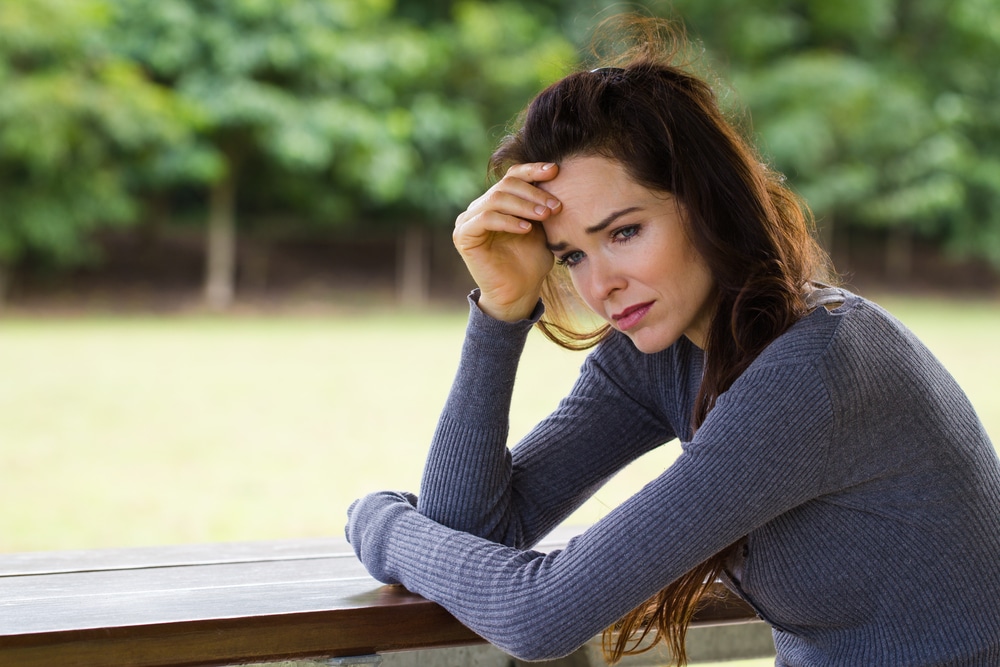 A sad and worried woman sitting down alone outdoors
