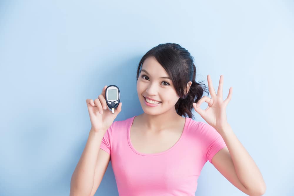 Woman holding a blood glucose meter to prevention diabetes isolated on blue background, asian