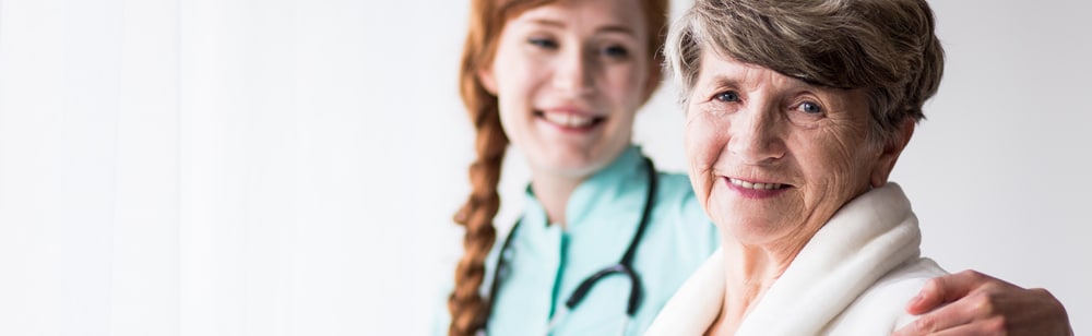 Supportive senior care assistant and smiling older woman in nursing home