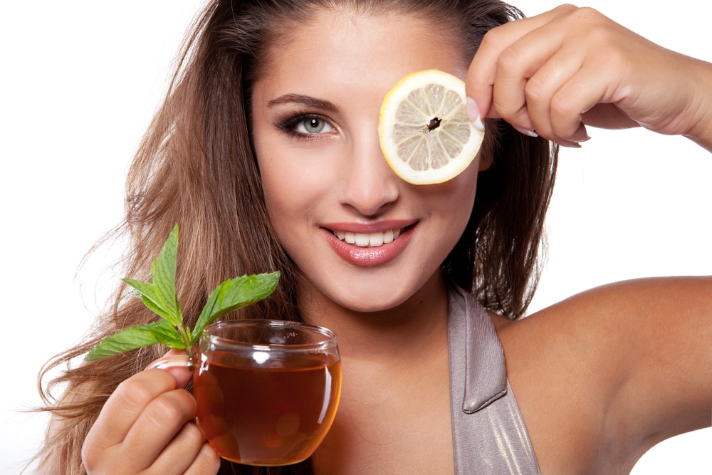 Woman with cup of fresh tasty black tea, mint and lemon
