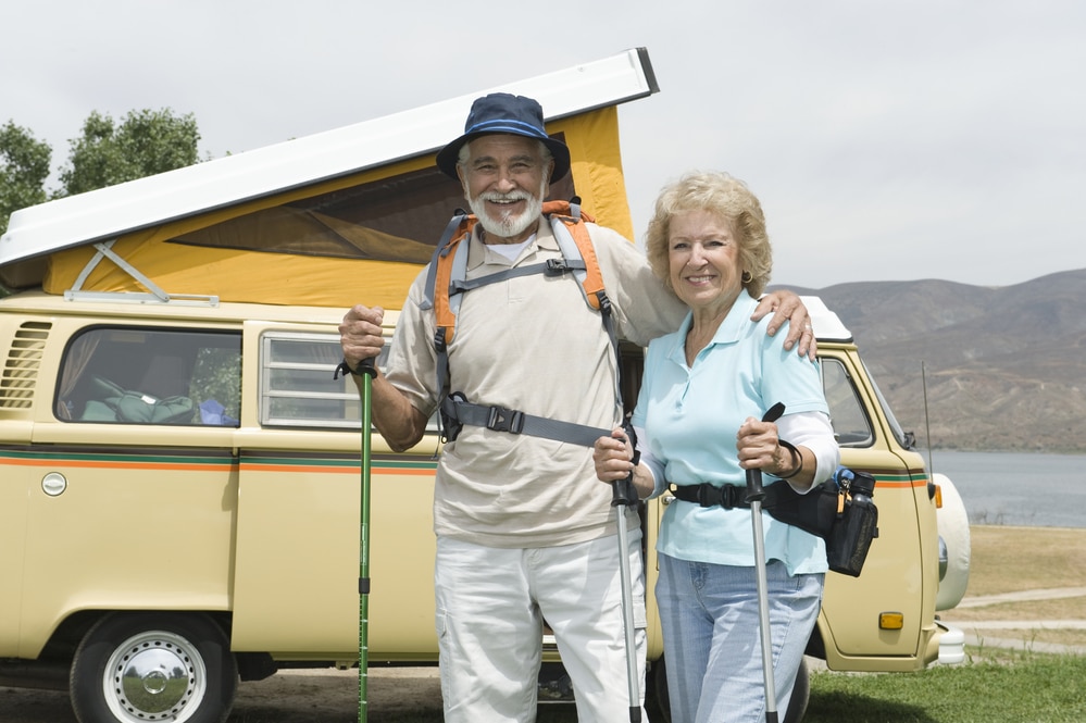Portrait of a happy senior Caucasian couple holding fishing rods with van in the background