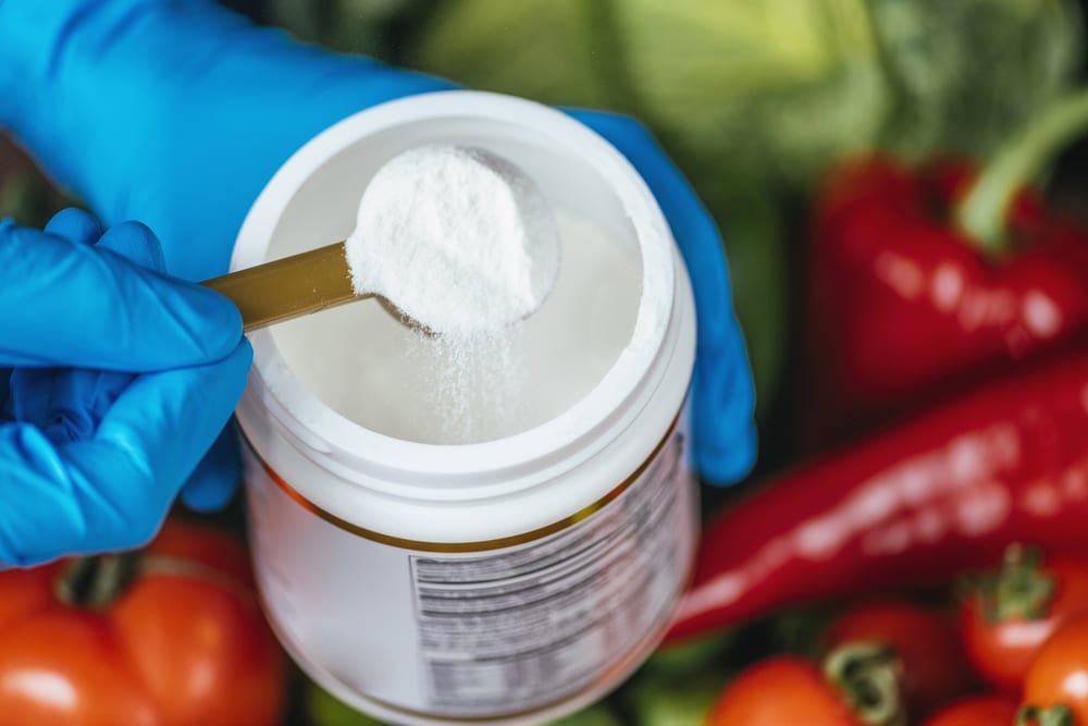 Collagen protein supplements powder in container with plastic spoon and fresh colorful vegetables on the table. Health and beauty supplement concept